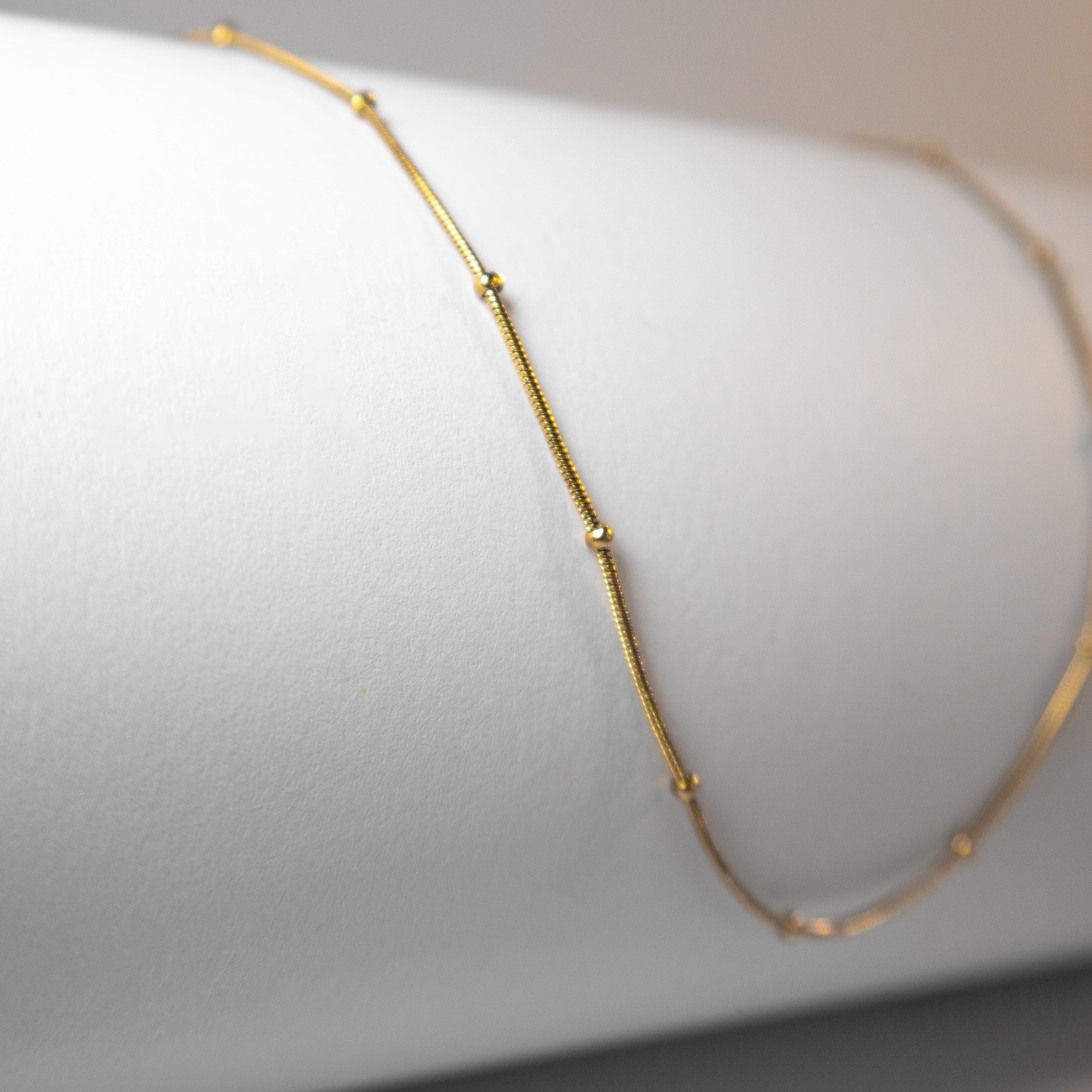 Gold beaded chain necklace arranged symmetrically on white studio background
