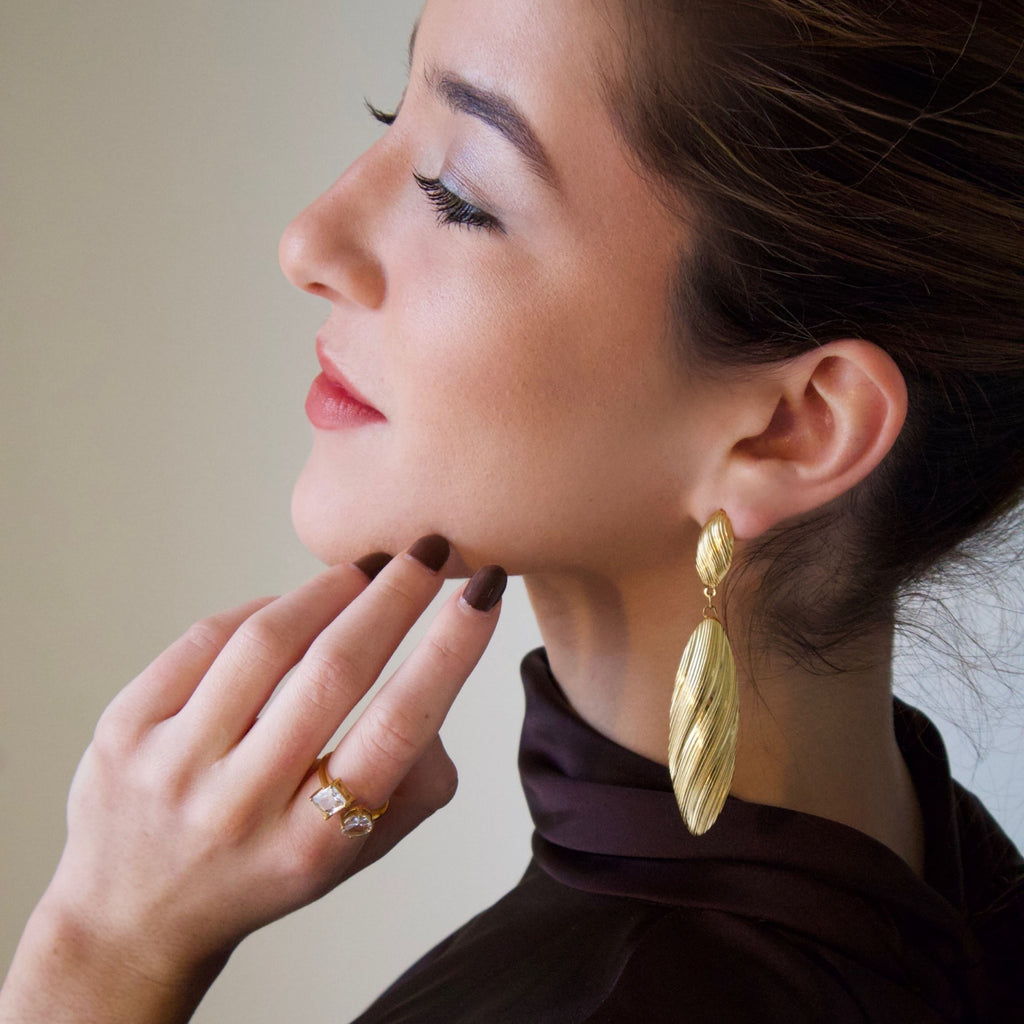Gold long drop earrings worn on ear, featuring elongated textured sculptural design
