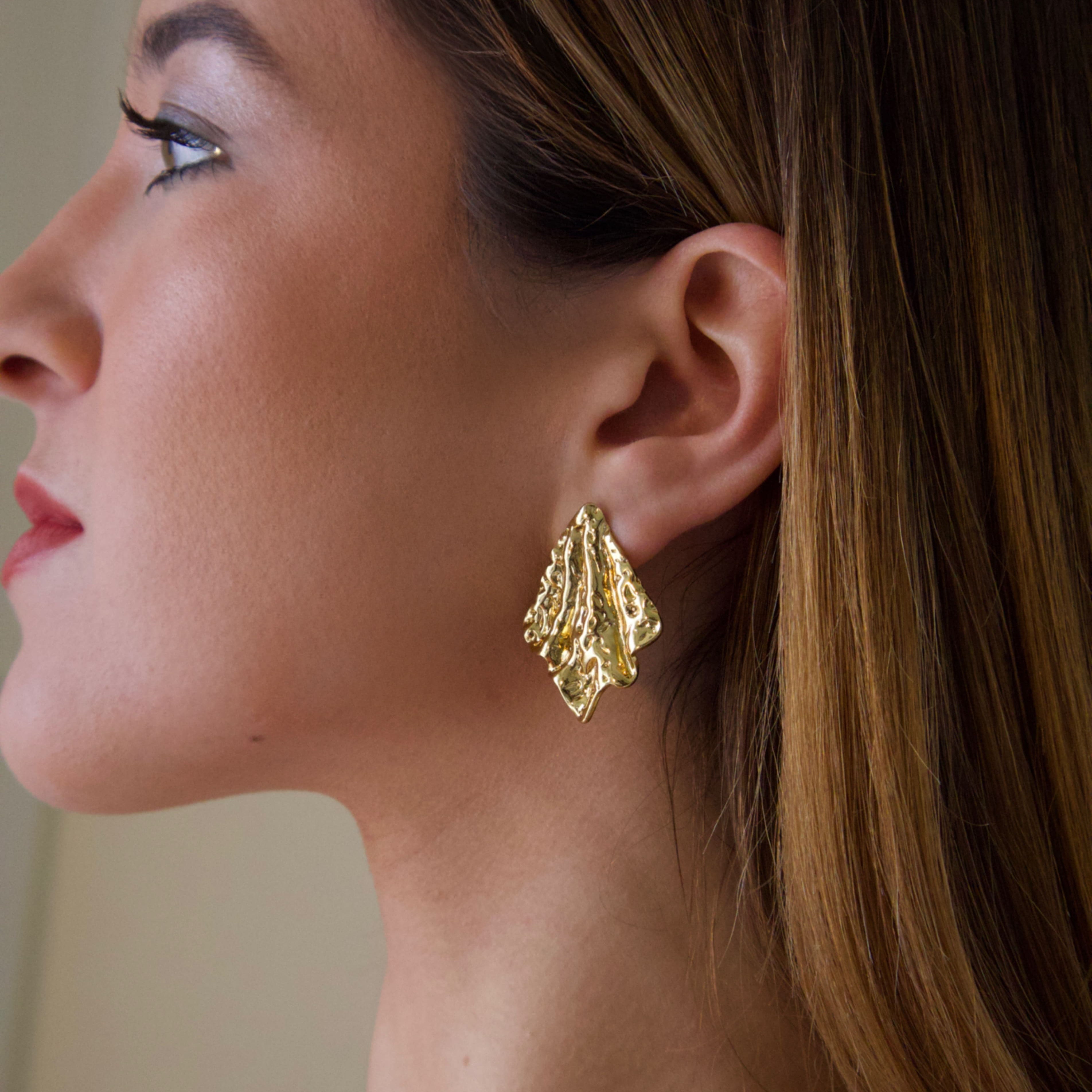 Gold sculptural statement earrings worn on ear with organic textured design
