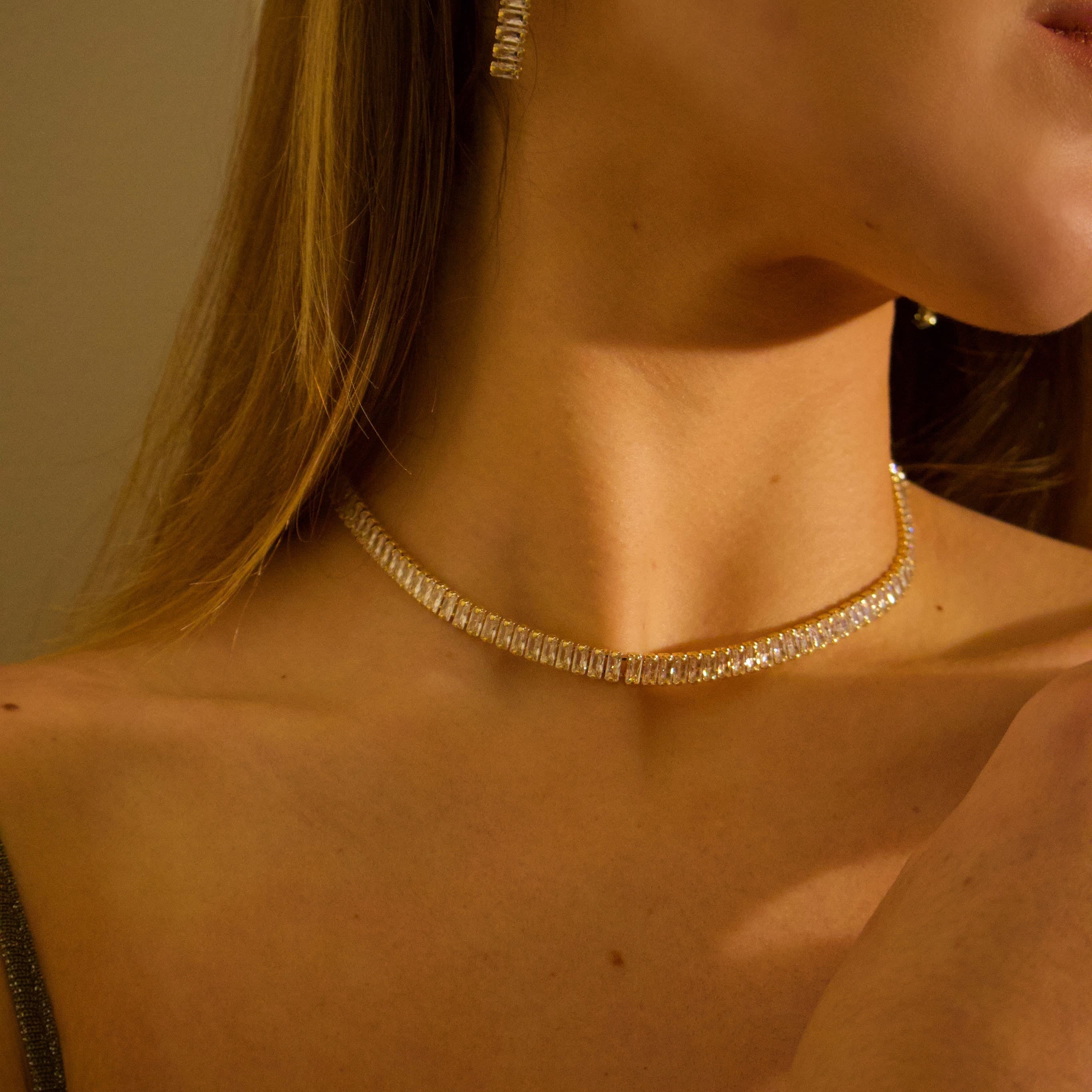 Gold tennis necklace with crystal stones worn around the neck
