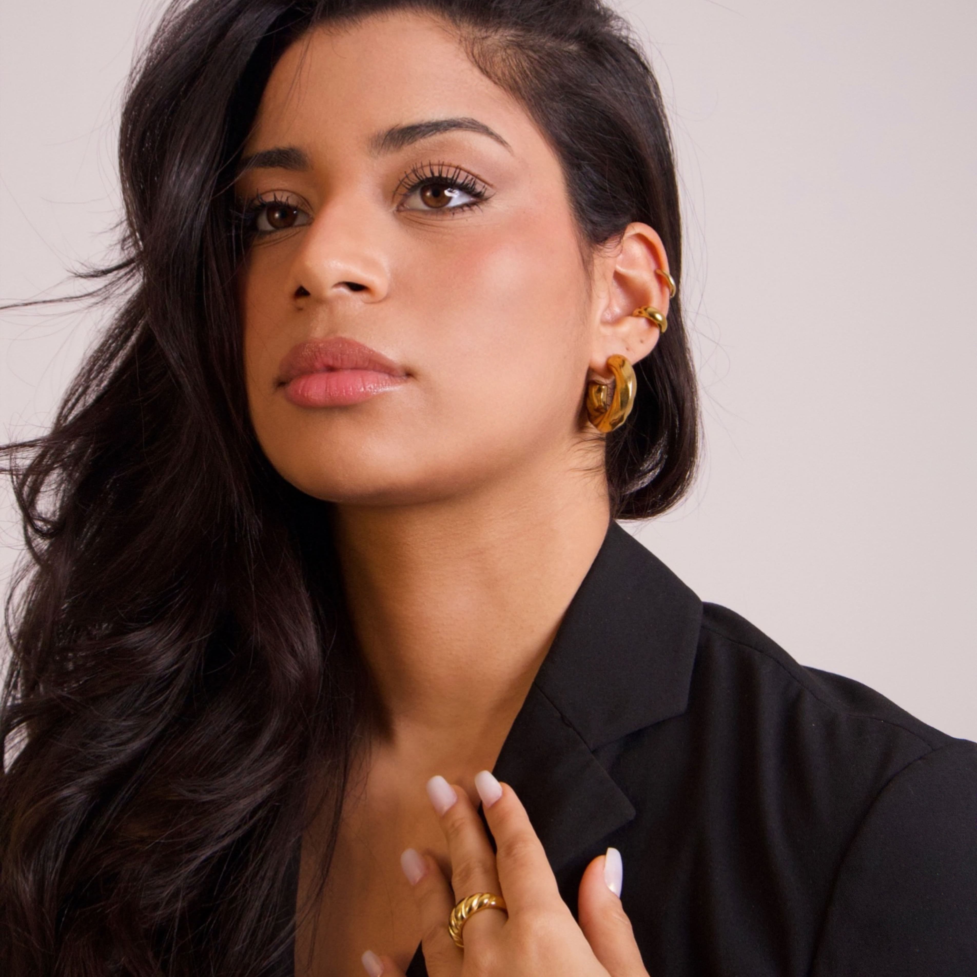 Model wearing sculptural gold earrings styled with a black blazer in a minimalist editorial look
