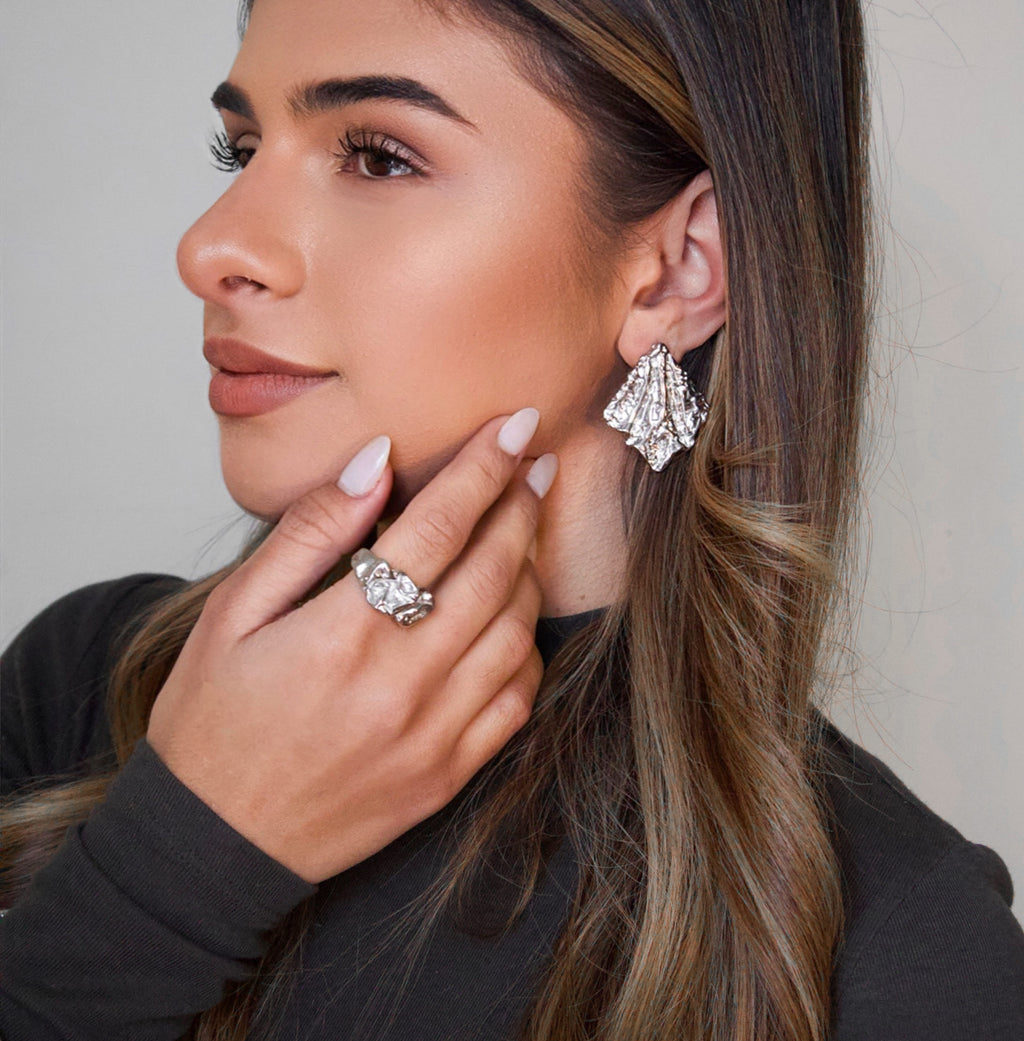 Silver statement earrings worn on ear with textured sculptural design
