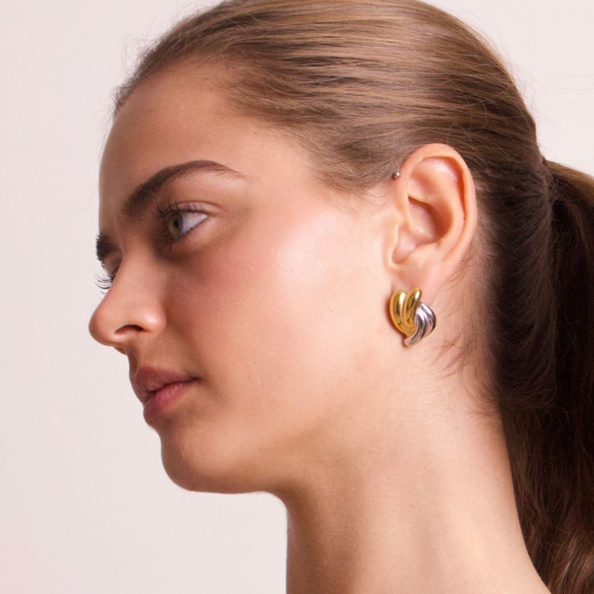Two tone gold and silver sculptural stud earrings worn by model in side profile
