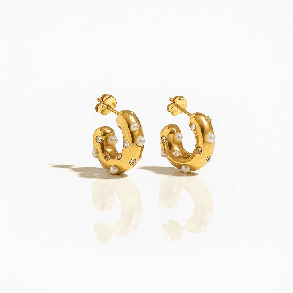 Elegant gold hoop earrings adorned with small pearls and crystals, modern luxury jewelry with a sculptural design on a white background.